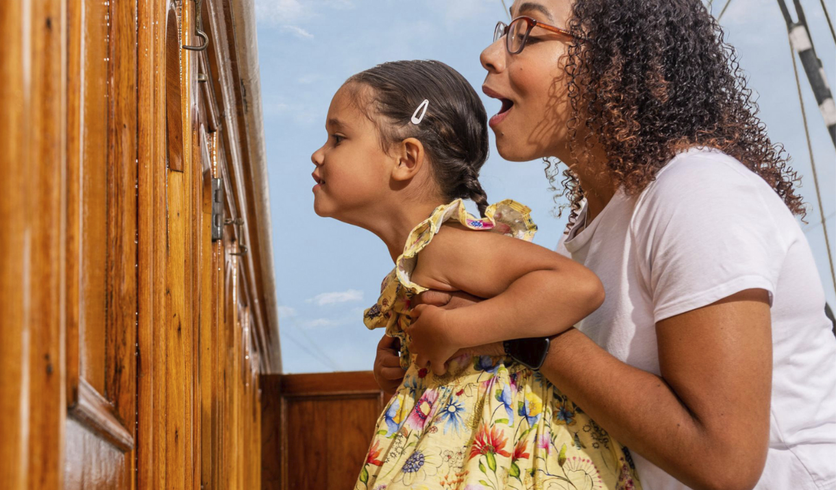 Mother holds up her daughter to look through a porthole on Cutty Sark in Greenwich